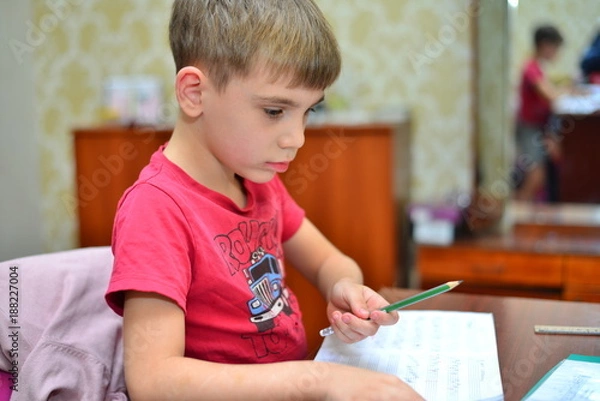 Fototapeta A child of primary school age do homework. The boy does his homework at his desk at home. The student / pupil has been bored on the lesson. Boy fell asleep during homework. Lovely first grader.