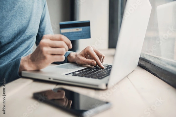 Obraz Man holding credit card and using laptop. Online shopping, business and technology concept.