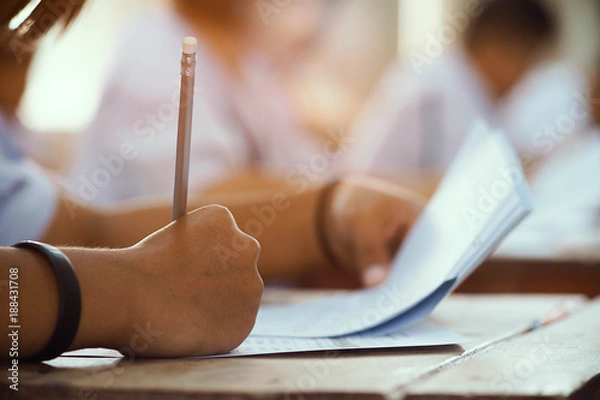 Fototapeta Closeup to hand of student  holding pencil and taking exam in classroom with stress for education test.