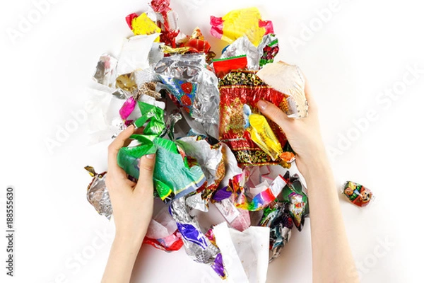 Fototapeta Hands holding a bunch of candy wrappers on a white background. Closeup