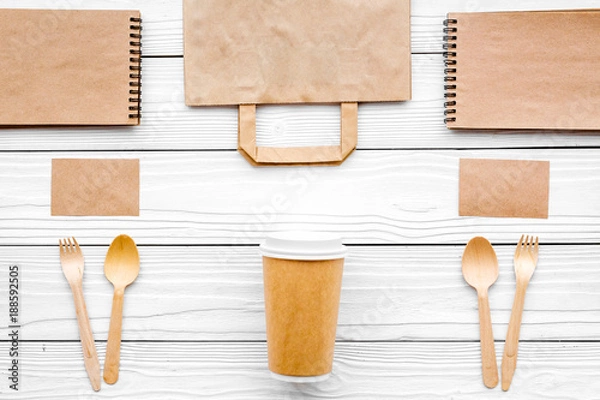 Fototapeta Set of recycle brown paper bag, disposable tableware cup, spoon, fork, notebook on white wooden background top view pattern