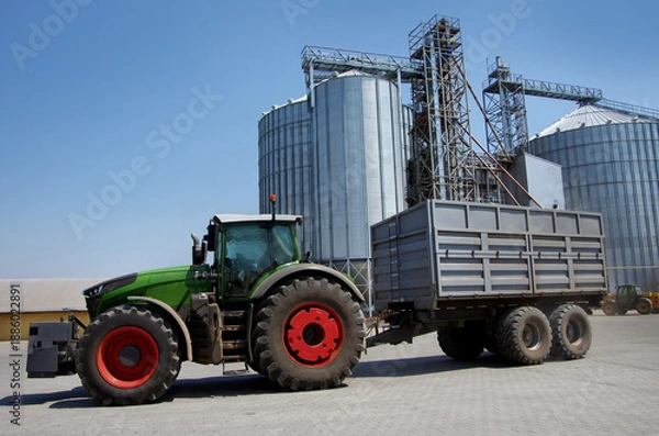 Obraz large tractor with cargo trailer near grain silos at elevator complex