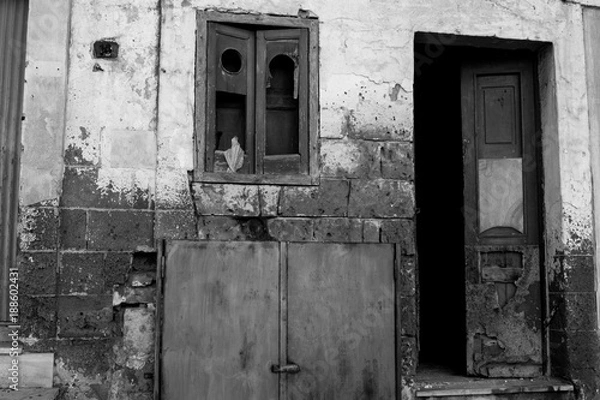 Fototapeta Ruined and Broken Facade With an Open  Door and a Window With a Broken Glass