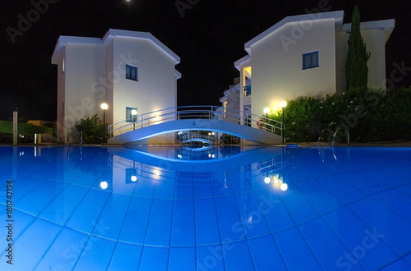 Obraz Бассейн с голубой водой и подсветкой в вечернее время, здания (корпуса) на заднем фоне