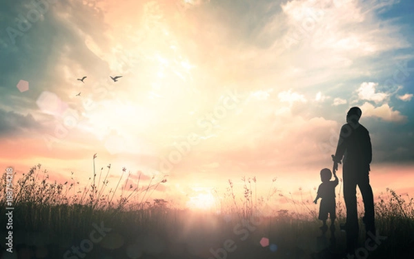 Obraz International migrants day concept: Silhouettes father and son holding hand in hand on meadow autumn sunset background