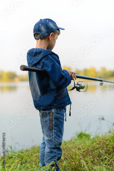 Obraz A fisherman boy on the river bank with a fishing rod in his hands. He wants to catch a big fish..