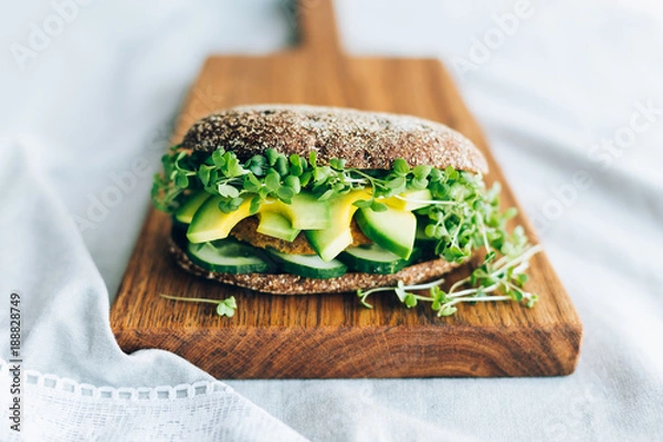 Obraz Vegetarian burger with cucumber, avocado, microgreen mustard on a wooden board