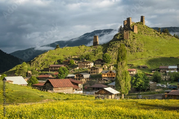 Fototapeta Scenic landscape of early summer morning in the depths of the Caucasus mountains. Sun just came out and illuminates ancient ruins of tushetian towers. Below the ruins is the village Upper Omalo.