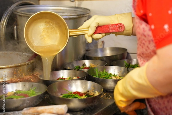 Fototapeta 전통시장 맛집 주방에서 커다란 양은 국자로 진하게 우려낸 육수를 칼국수 그릇에 담아내는 정겨운 모습