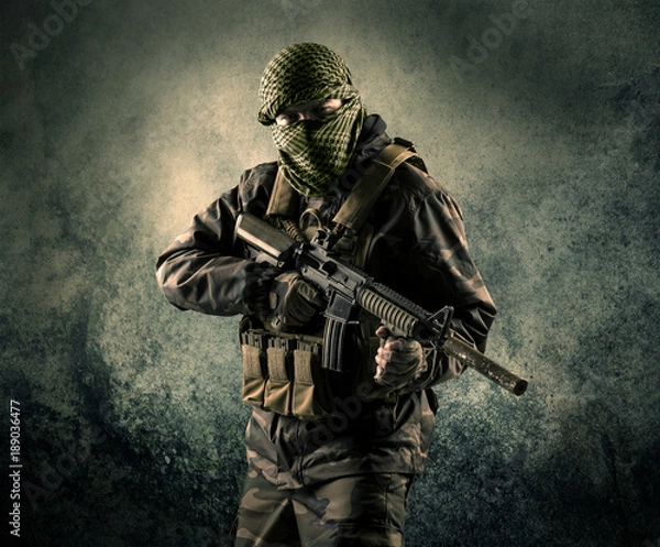 Fototapeta Portrait of a heavily armed masked soldier with grungy background