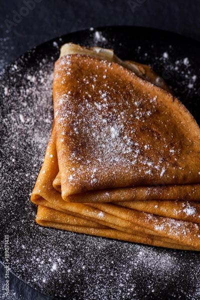 Fototapeta Stack of crepes with powdered sugar on dark background. Maslenitsa. Russian folk festival