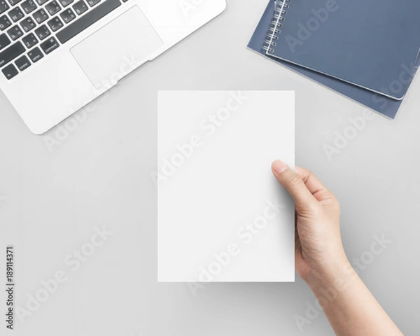 Fototapeta Hand women holding blank paper A4 size on office table top view.