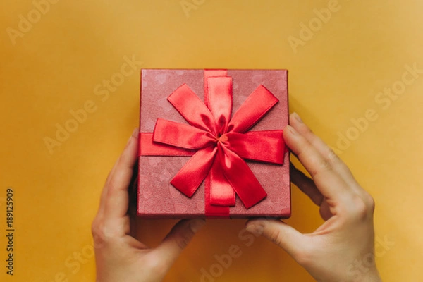 Fototapeta The girl has received a gift in a beautiful red box with a ribbon and is going to open it.