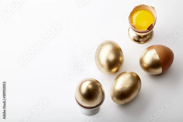 Fototapeta Eggs painted golden with yolk in egg stand on white background. Easter tradition concept, copy space