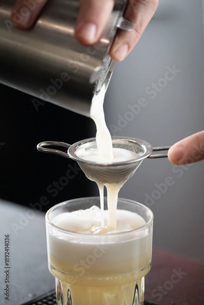 Obraz Barman filtering egg while preparing pineapple whisky sour. Emphasizes cleanliness, texture refinement, and precise mixology skill.