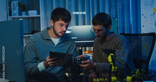 Obraz Team adult male engineer collaborate on robotic hand project using AI code solutions machine learning at tech workspace night. Artificial intelligence interface, collaboration prototype development.