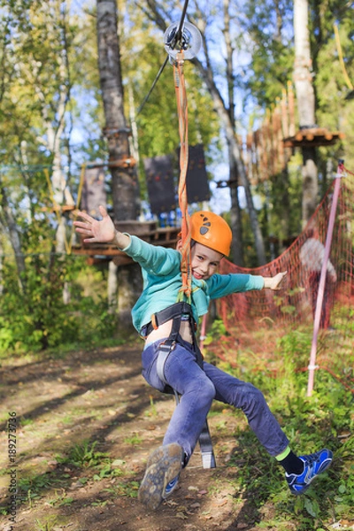 Fototapeta happy boy on zip line. cheerful kid in adventure park. vertical 