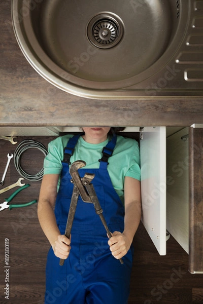 Fototapeta kobieta w niebieskim kombinezonie z regulowanym kluczem pod umywalką widok z góry