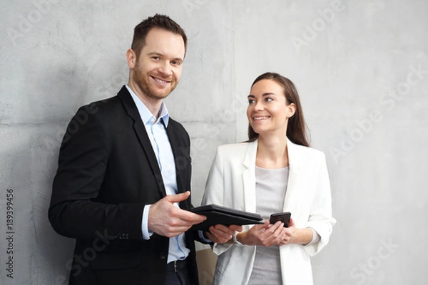 Obraz Spotkanie biznesowe. Młodzi pracownicy biurowi stoją na korytarzu w firmie i czytają tablet.