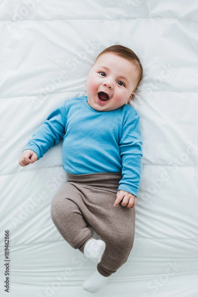 Fototapeta Portrait of an adorable 3 month old baby smiling lying in a bed of white sheets