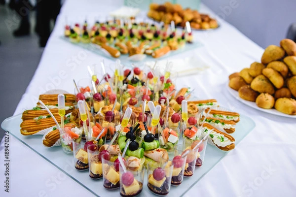 Obraz Beautifully decorated catering banquet table with burgers and profiteroles. Variety of tasty delicious snacks on the table