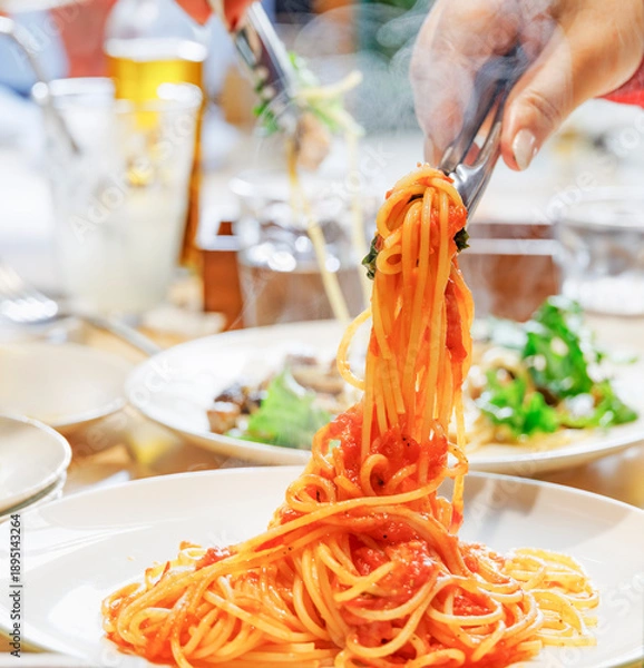 Obraz トングで高く持ち上げられた湯気が立つ熱々のトマトソーススパゲッティ