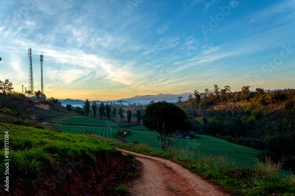 Fototapeta Mountain path and telecommunication tower on top of the mountain whit colorful sky at sunrise or sunset time.