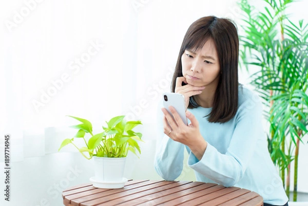 Obraz 困った顔をしてスマートフォンを使う女性