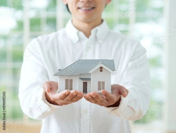Obraz 両手で家の模型を大切に持つ男性が伝える住宅購入と安心の暮らしイメージ
