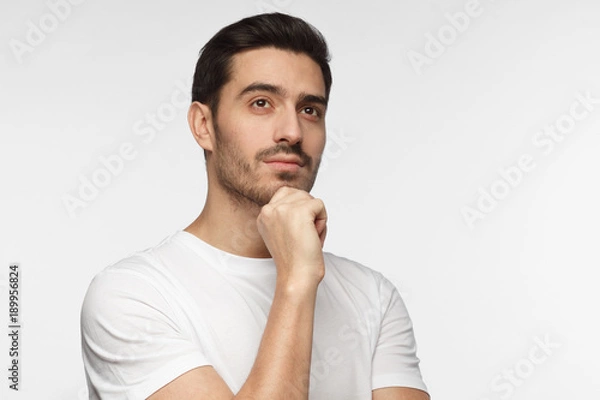 Fototapeta Portrait of young man with dreamy cheerful expression, thinking, isolated over gray background with copy space for your text