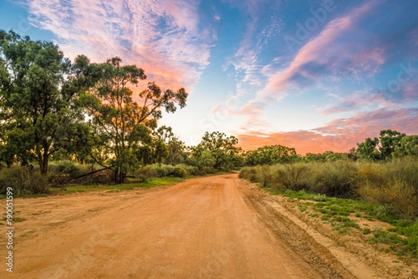 Obraz Wiejski krajobraz Australii z kolorowymi chmurami i polną drogą żwirową w Outback w Australii o wschodzie / zachodzie słońca