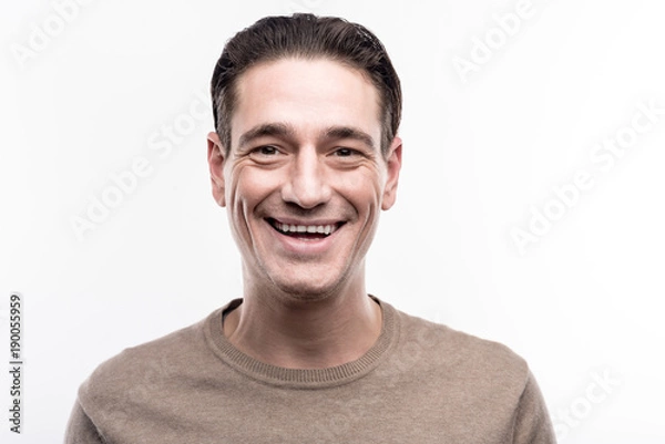 Fototapeta Lovable smile. The portrait of a pleasant middle-aged man posing for the camera and smiling while standing isolated on the white background