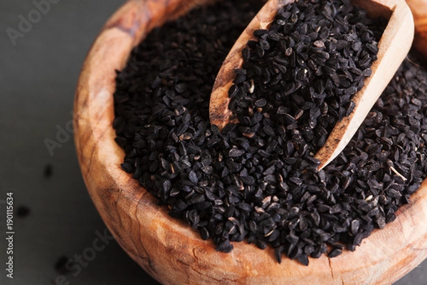 Fototapeta Black cumin or nigella sativa or kalonji seeds in bowl with spoon on black slate background, selective focus