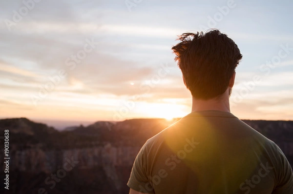 Fototapeta A man standing, looking out at the Grand Canyon during sunset. 