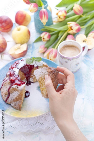 Obraz A bouquet of fresh tulips. Sweet home cupcake with sugar. Coffee in a cup. Apples on the table. The hand holds the cupcake.