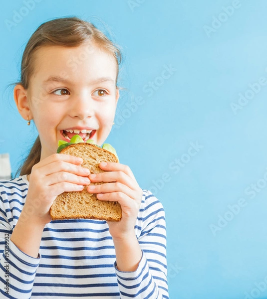 Obraz Little smiling girl eating an healthy sandwich with salad and avocados