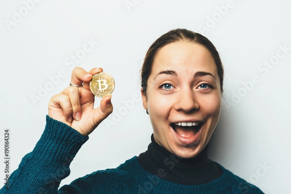 Fototapeta Young happy smiling girl shows Golden Bitcoin coin in hand - symbol of cryptocurrency, new virtual money
