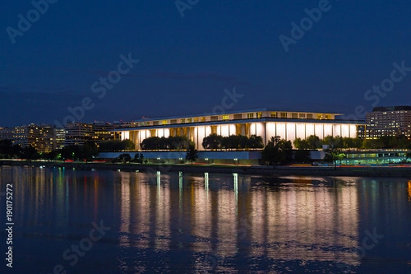Fototapeta Nocna panorama Waszyngtonu DC z John F. Kennedy Center for the Performing Arts w środku kadru. Jasno oświetlone Centrum Kennedy'ego z odbiciem w ciemnych wodach rzeki Potomac.