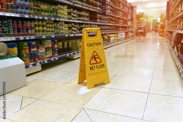 Fototapeta Żółty znak - uwaga. Mokra podłoga w supermarkecie na tle rozmytych produktów stojących na półkach