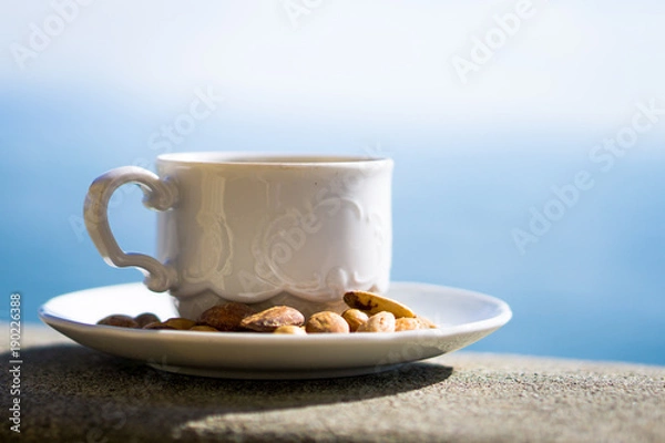 Fototapeta Cup of coffee with decorative nuts, with lake in soft focus in the background