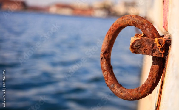 Fototapeta Rusty bollard waits at quay for a boat to be tied. Blur sea for background, closeup, details, banner