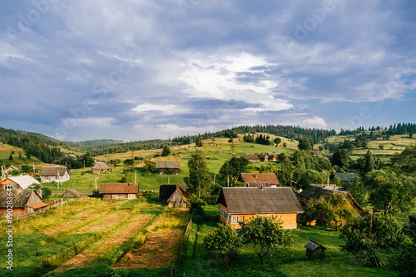 Fototapeta Countryside rural nature landscape in summer sunny day. Discover Ukraine. Village in Carpathians mountains. Beautiful scenic view at green hills and rustic terrain. Farmer houses in forest territory.