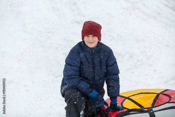 Fototapeta kid sledding from a hill, makes snowballs and snowman on his winter holidays
