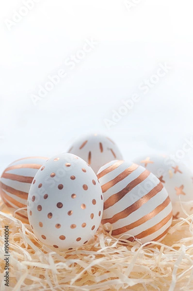 Fototapeta Golden Easter eggs in straw nest on white wooden rustic vintage background.