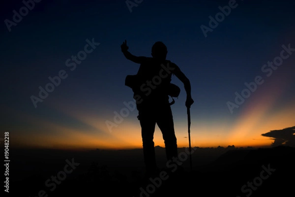 Fototapeta Silhouette of man hiking on top mountain trees forest with light during sunset, winter season