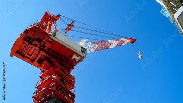 Obraz 雲ひとつない青空の下で建設作業を行う赤と白の大型タワークレーン