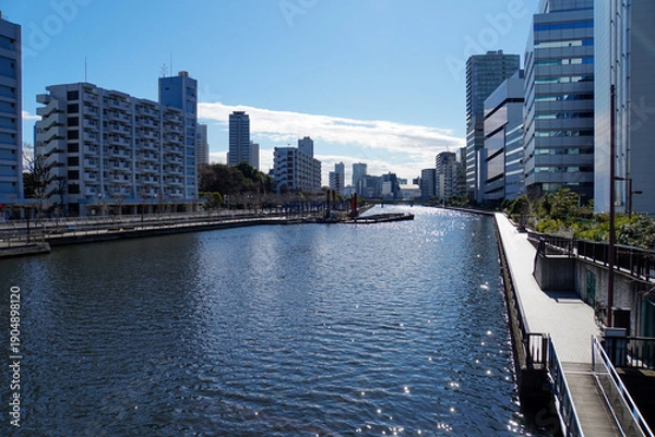 Obraz 晴天の下でキラキラと光る水面が美しい都市部を流れる運河と両岸に並ぶビル群