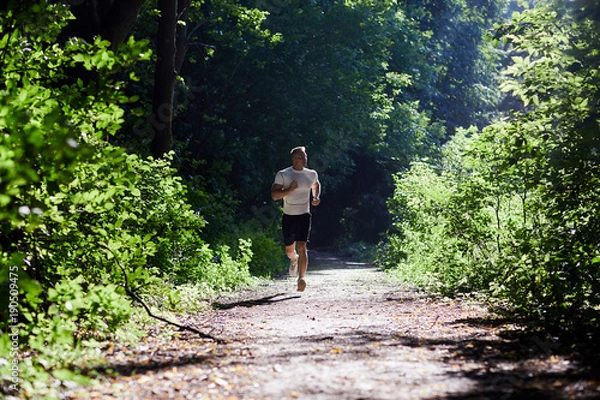 Obraz Sports man doing Jogging in the Park on the track in the morning at dawn.