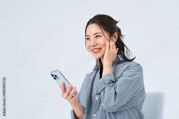 Obraz イヤホンを装着してスマートフォンを手にする若い女性
