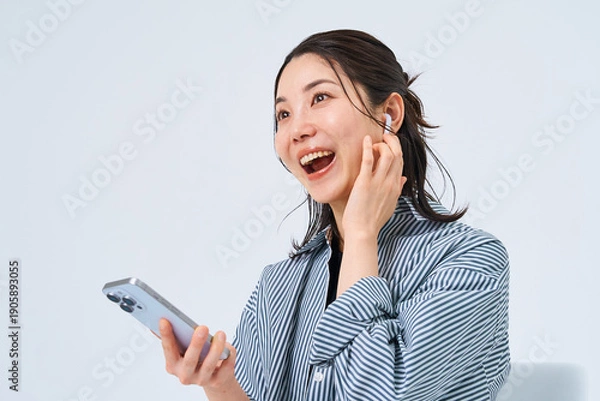 Obraz イヤホンを装着してスマートフォンを手にする若い女性